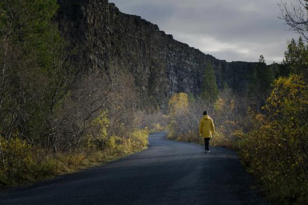 Person walking in the middle of a road surrounded by cliffs
