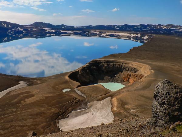Volcanic landscape with a large lake reflecting sky and a smaller turquoise crater lake.