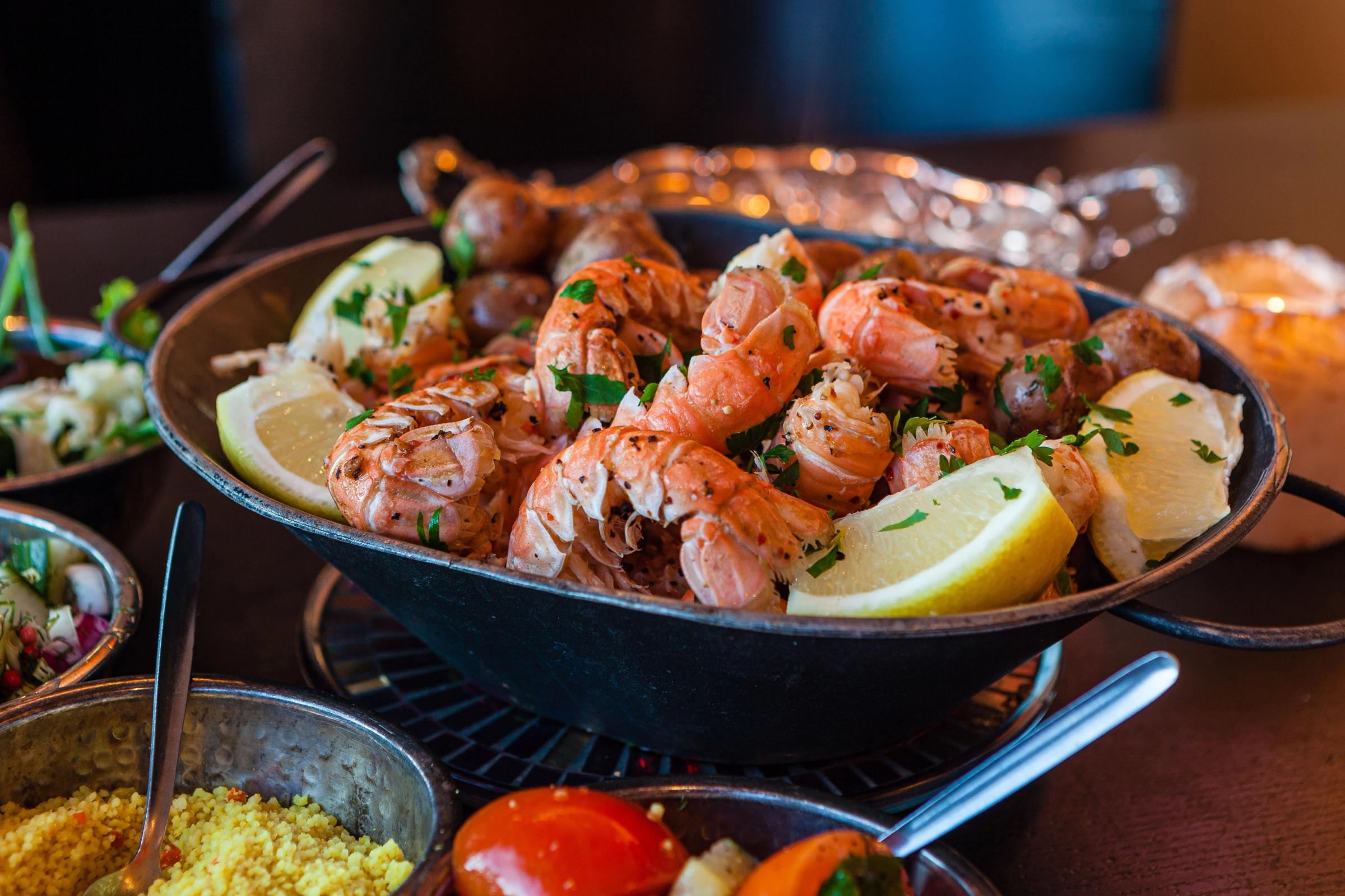 A pan of cooked shrimp, small potatoes, lemon wedges, and parsley, with side dishes.
