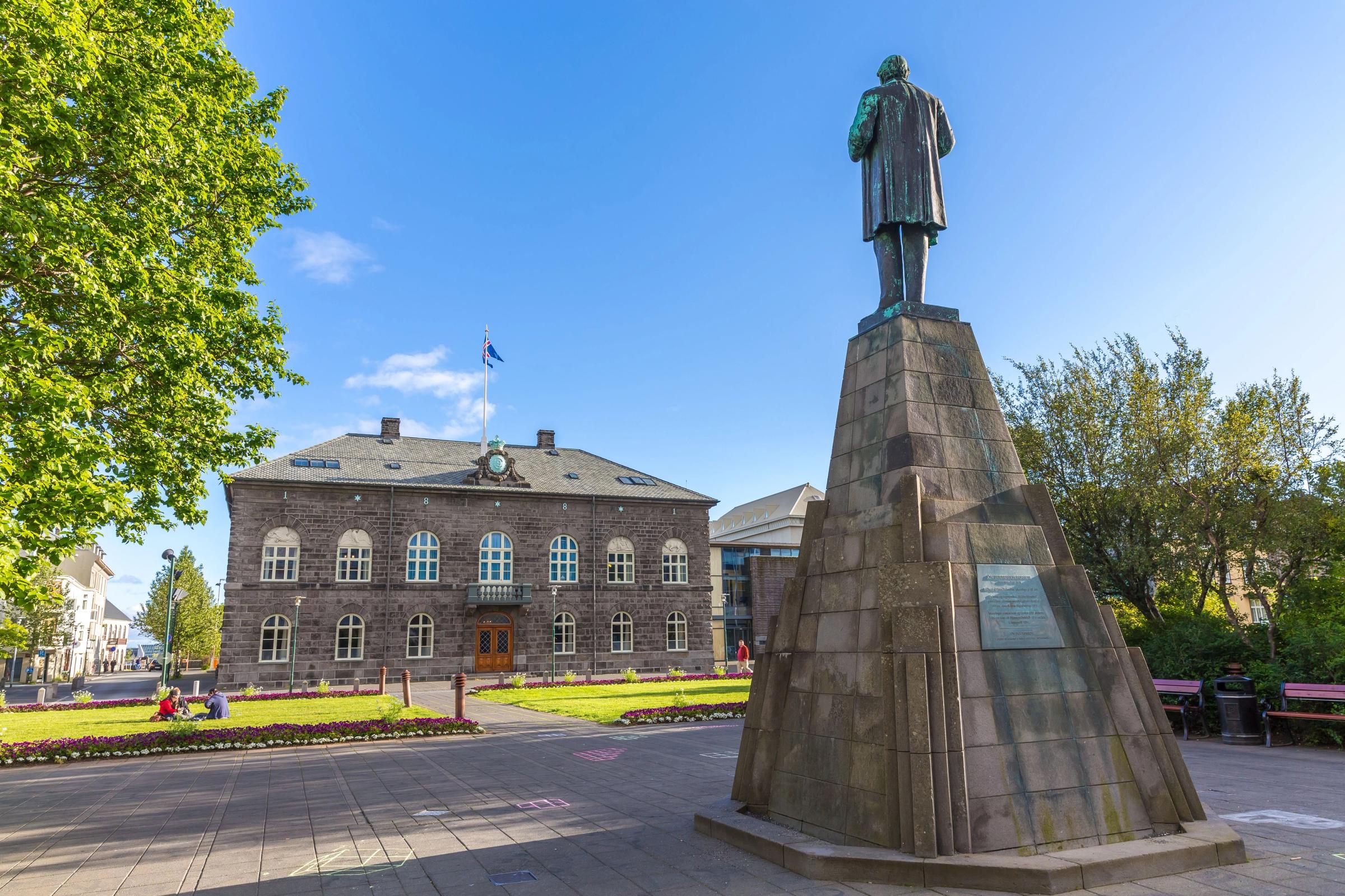 The Icelandic Parliament building and a large statue in a sunny park.