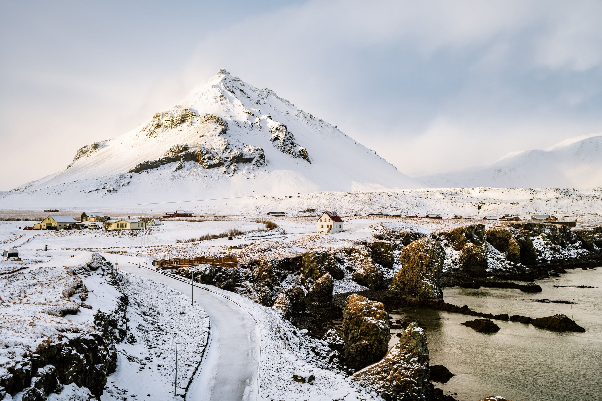 an aerial view of a snowy landscape with a mountain in the background at Arnarstapi in iceland.