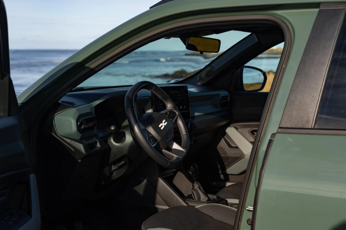 Interior do Dacia Duster visto através da porta aberta do condutor, com volante e vista para o mar