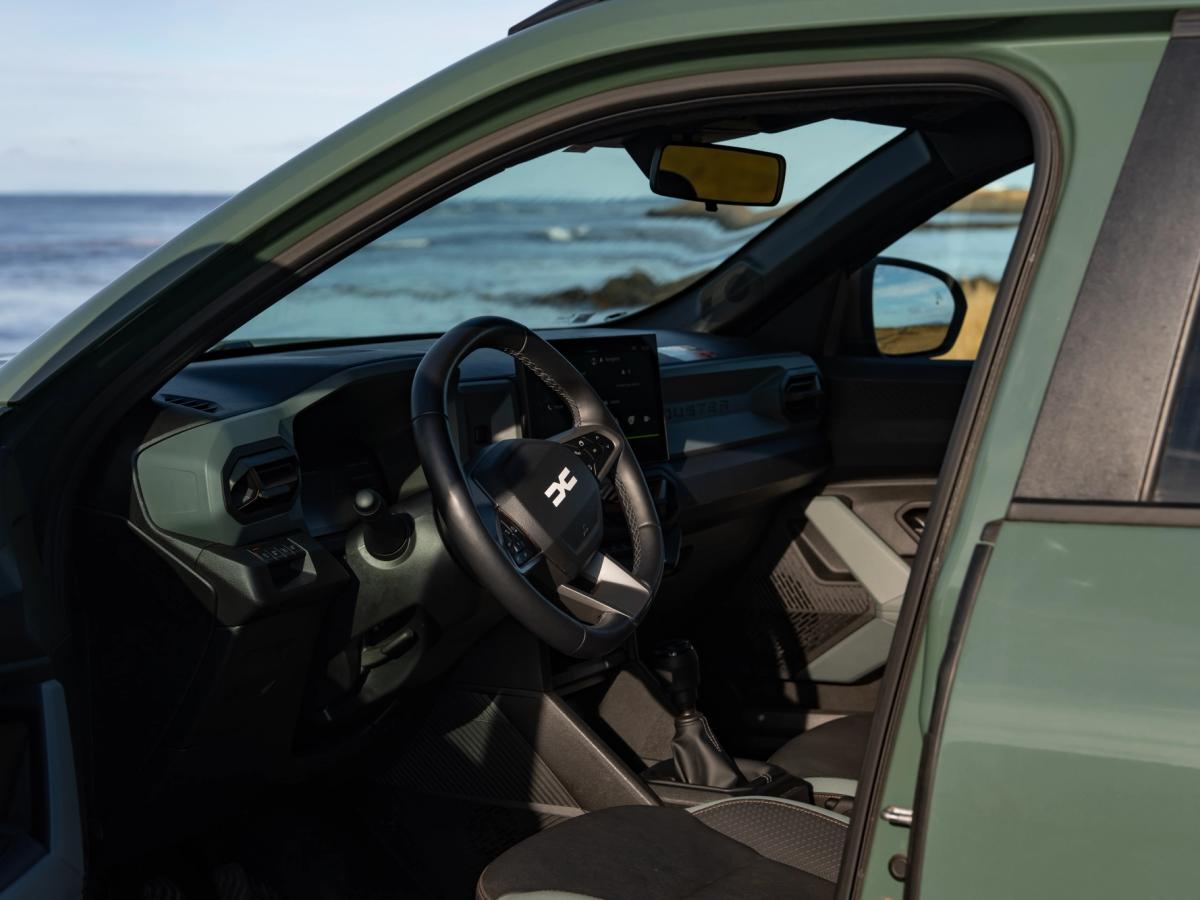Interior do Duster com a porta aberta Interior do Dacia Duster visto através da porta aberta do condutor, com volante e vista para o mar
