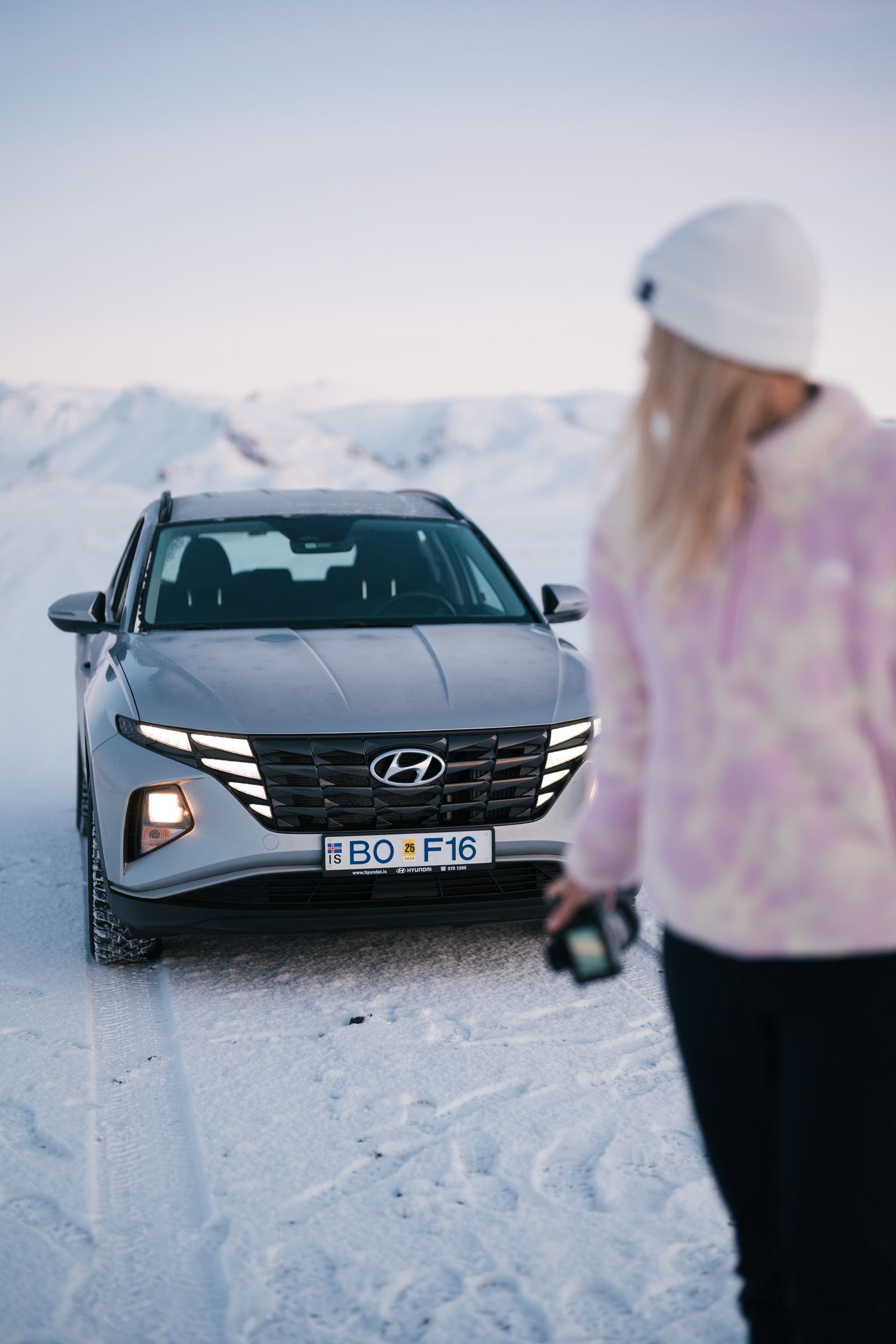 A grey Hyundai SUV on a snowy road with mountains in the distance, a person out of focus in the foreground.