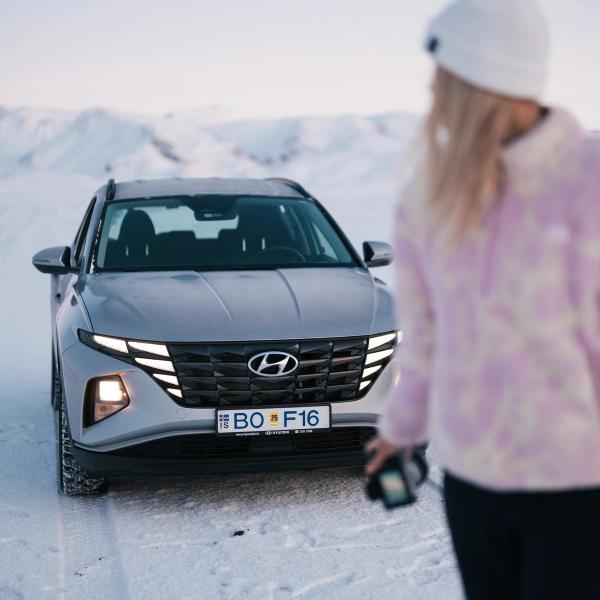 A grey Hyundai SUV on a snowy road with mountains in the distance, a person out of focus in the foreground.