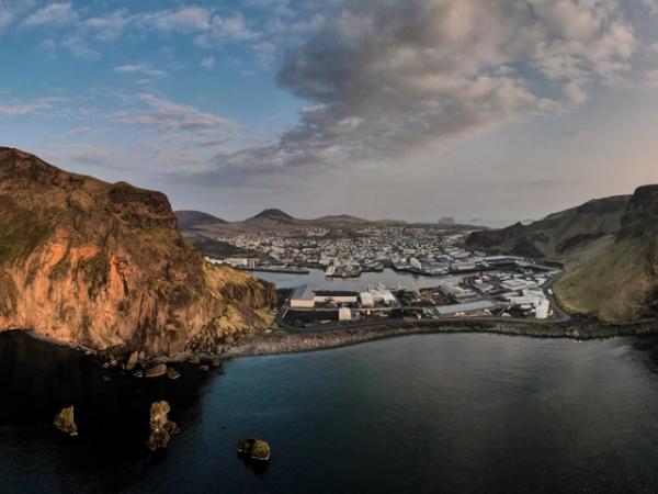 une vue aérienne d'une petite île au milieu de l'océan au coucher du soleil aux Îles Vestmann en Islande.