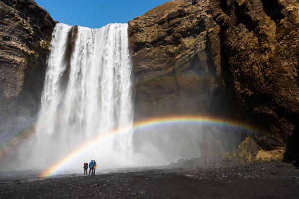 Three people in front of Skógafoss with a small rainbow