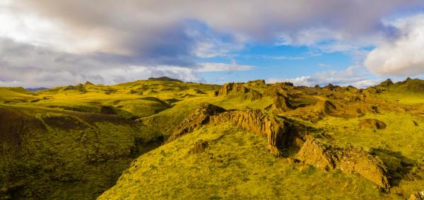 an aerial view of a lush green mountain landscape with a blue sky and clouds .
