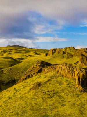 an aerial view of a lush green mountain landscape with a blue sky and clouds .