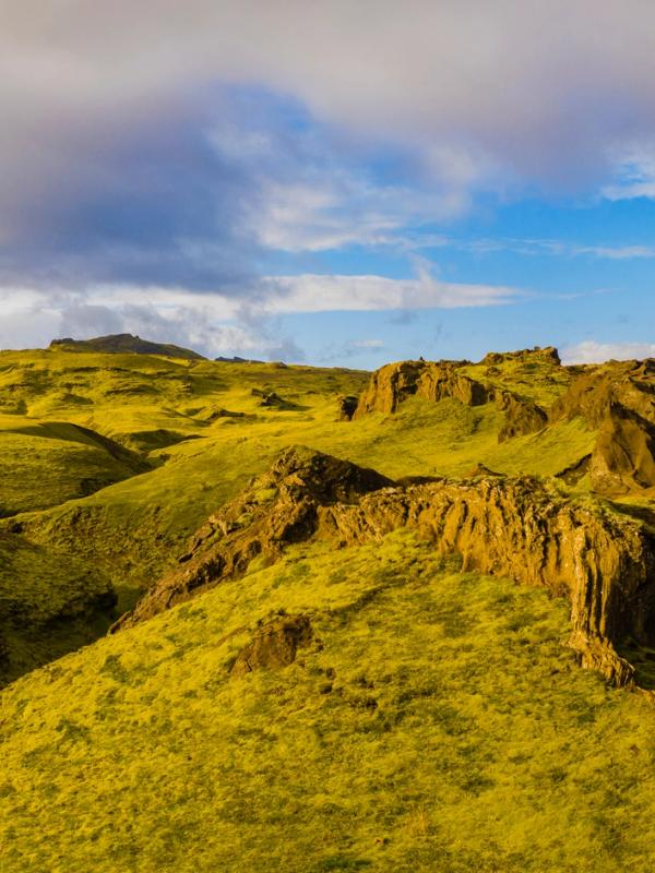 an aerial view of a lush green mountain landscape with a blue sky and clouds .