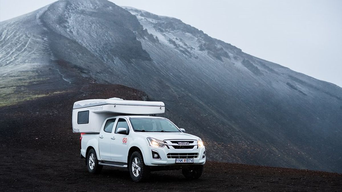 White camper truck on dark, rugged terrain with a snow-capped mountain in the background.