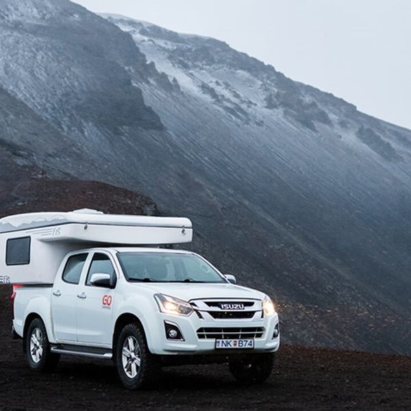 a white truck with a trailer on top of it is parked in front of a mountain .