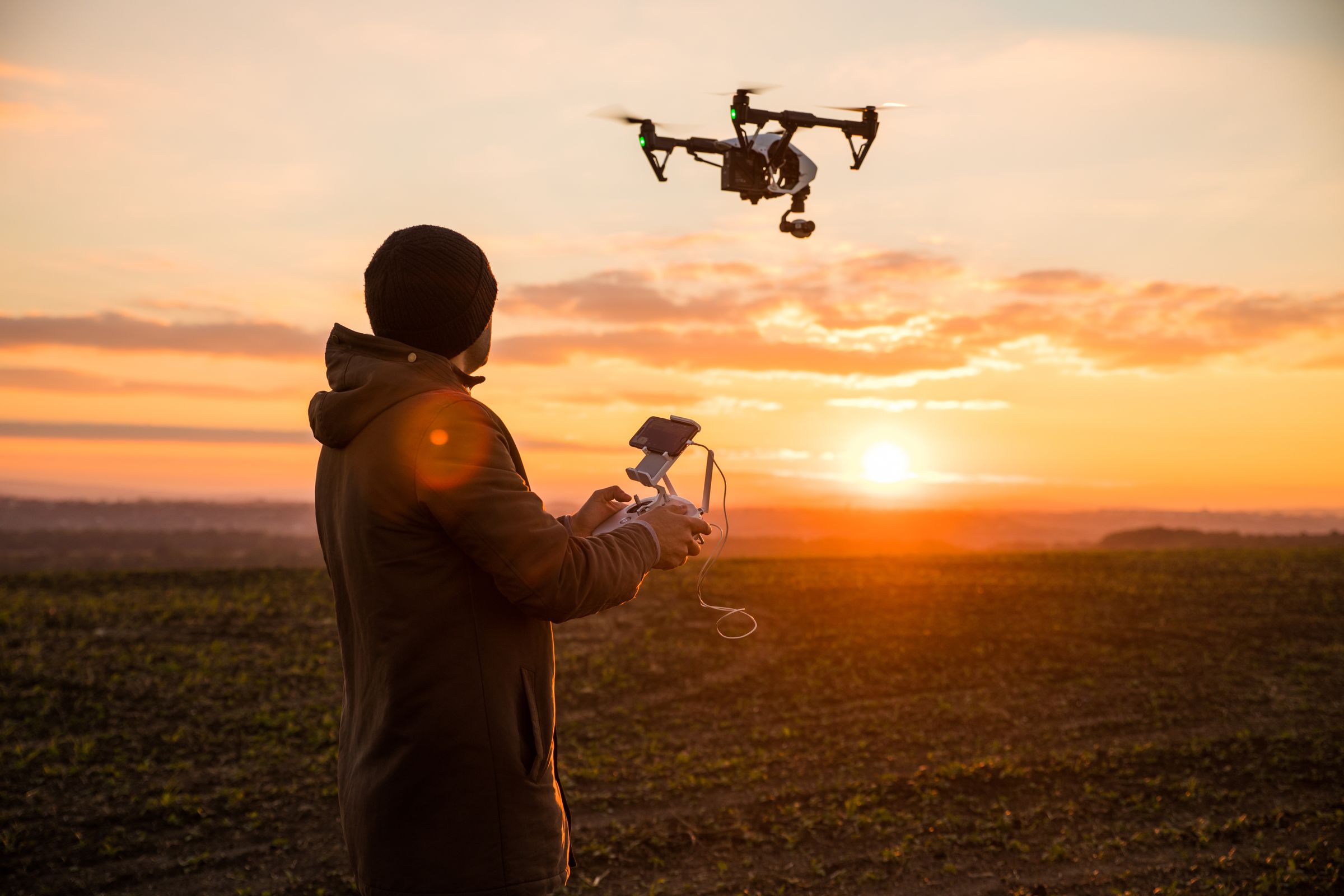 un hombre está volando un dron en un campo al atardecer.