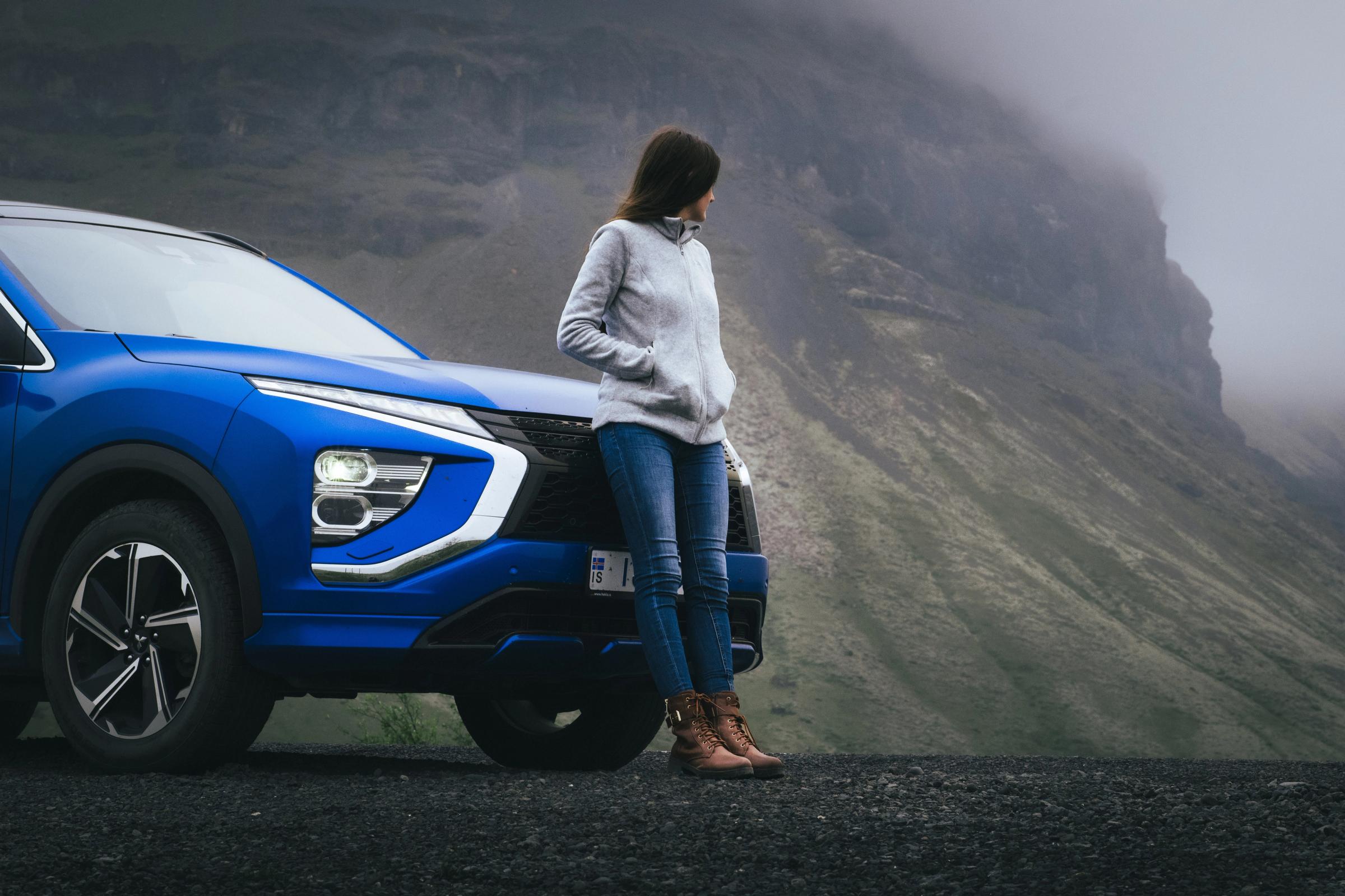 Vista frontal de un Mitsubishi Eclipse Cross con una persona apoyada en el capó junto a un acantilado cubierto de niebla