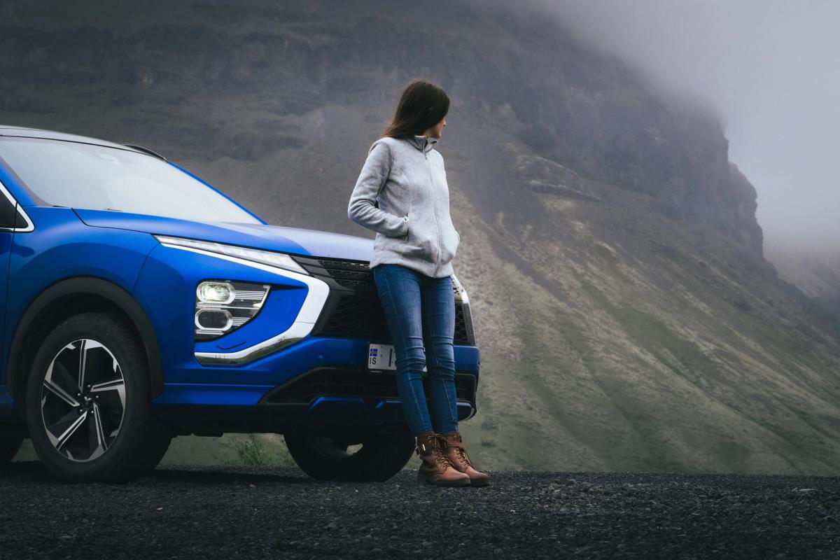 Vista frontal de un Mitsubishi Eclipse Cross con una persona apoyada en el capó junto a un acantilado cubierto de niebla