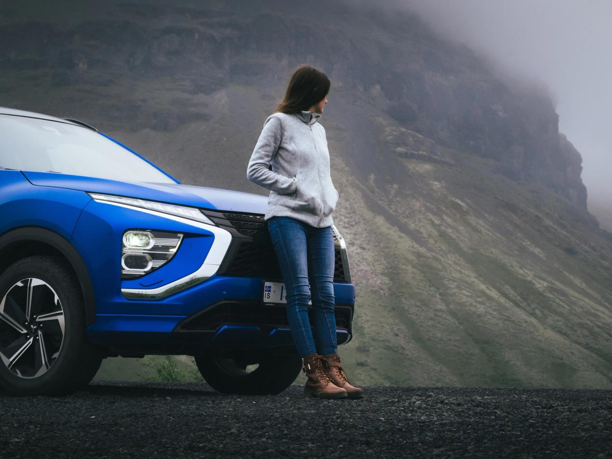 Mitsubishi Eclipse Cross con vistas al acantilado Vista frontal de un Mitsubishi Eclipse Cross con una persona apoyada en el capó junto a un acantilado cubierto de niebla