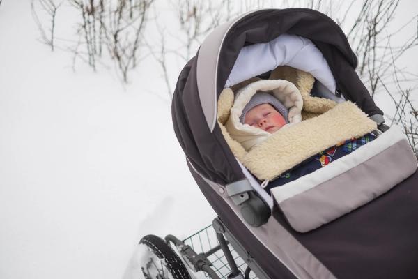 A baby bundled warmly and sleeping in a stroller in the snow.