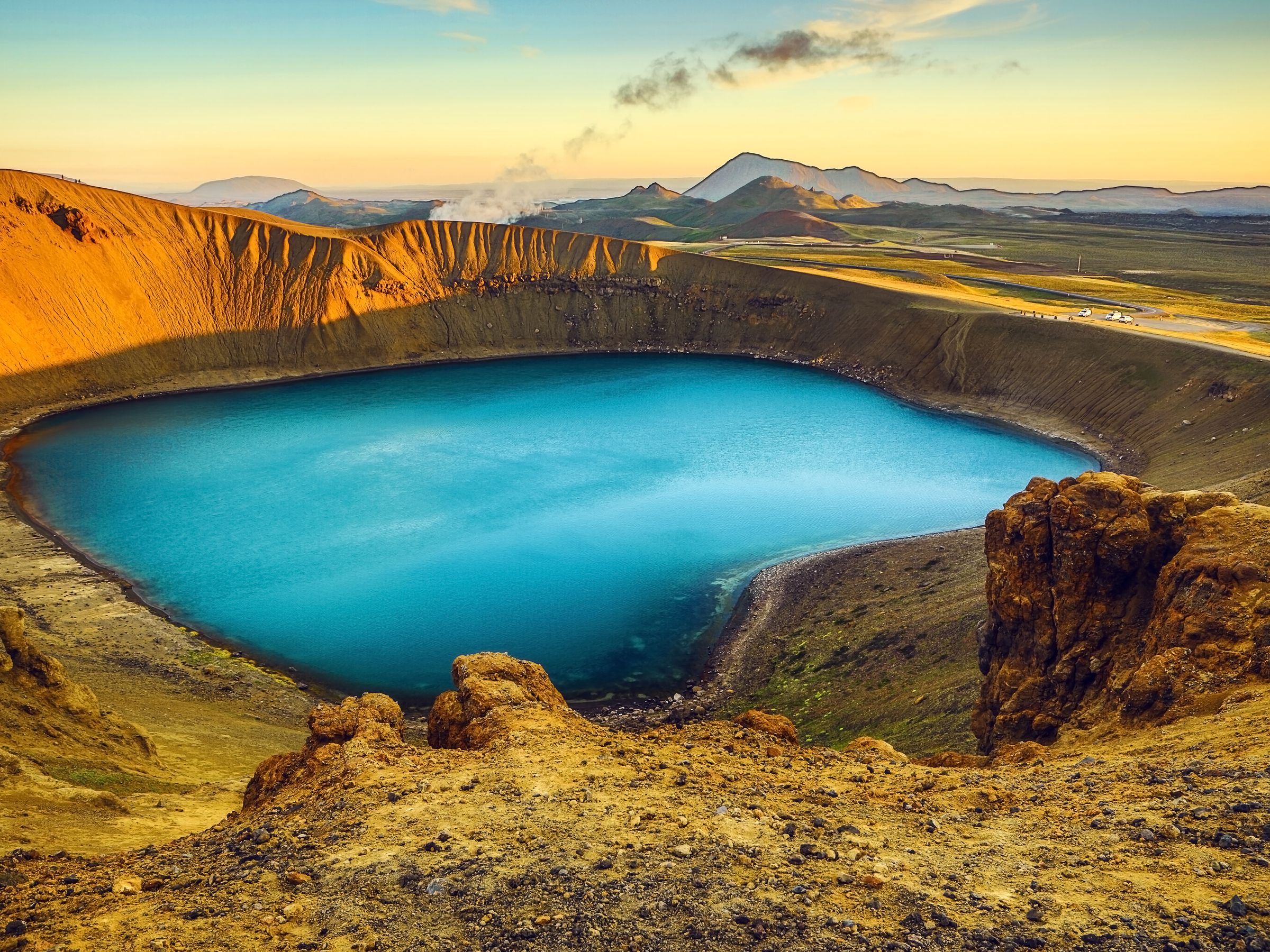 Vibrant blue crater lake surrounded by golden volcanic hills at sunrise.