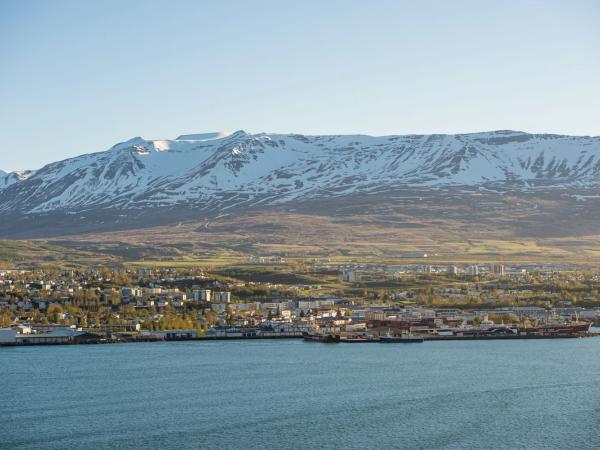 Panorámica de una ciudad al lado del mar, con barcos en su puerto y montañas nevadas de fondo