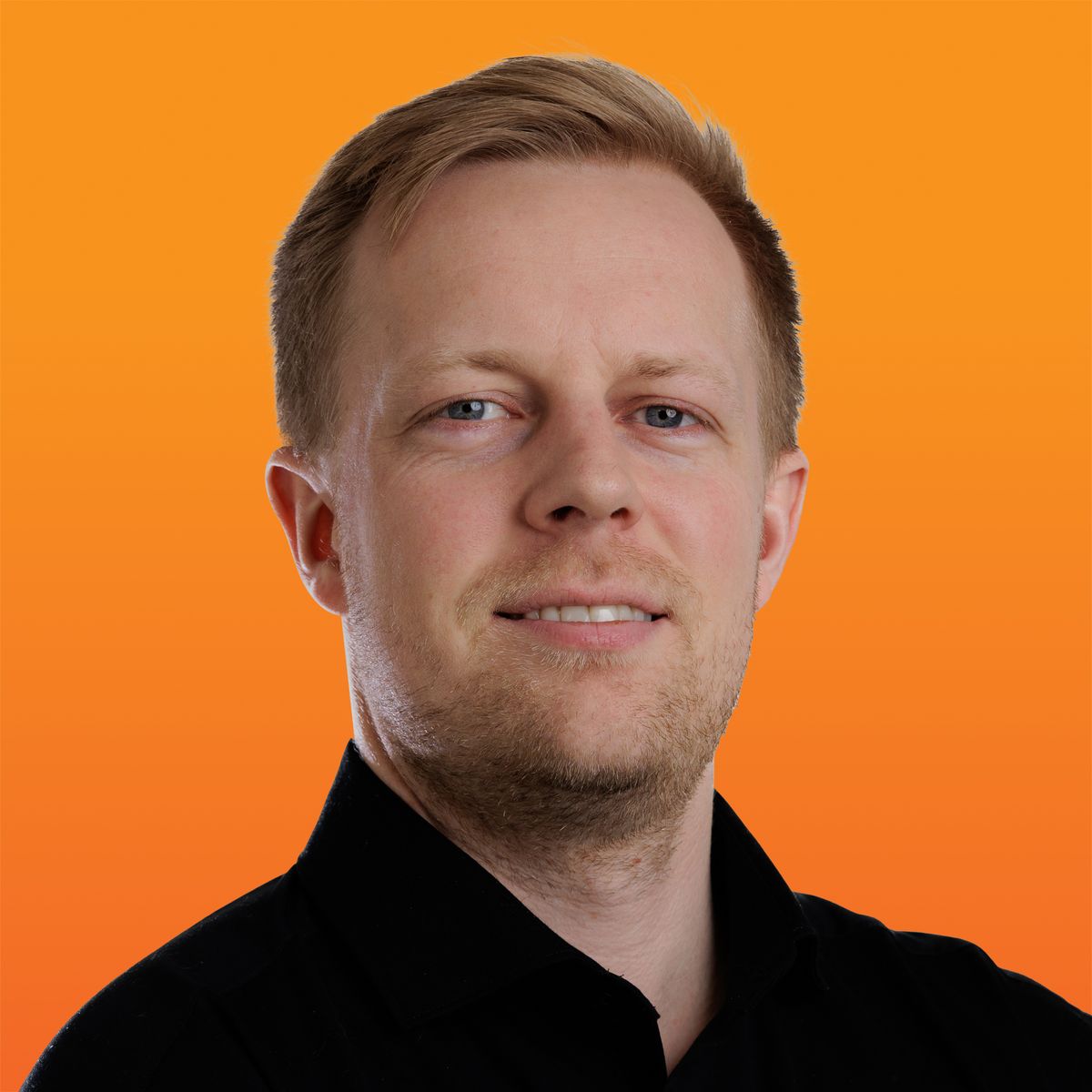 a man with a beard and a black shirt is smiling in front of an orange background .