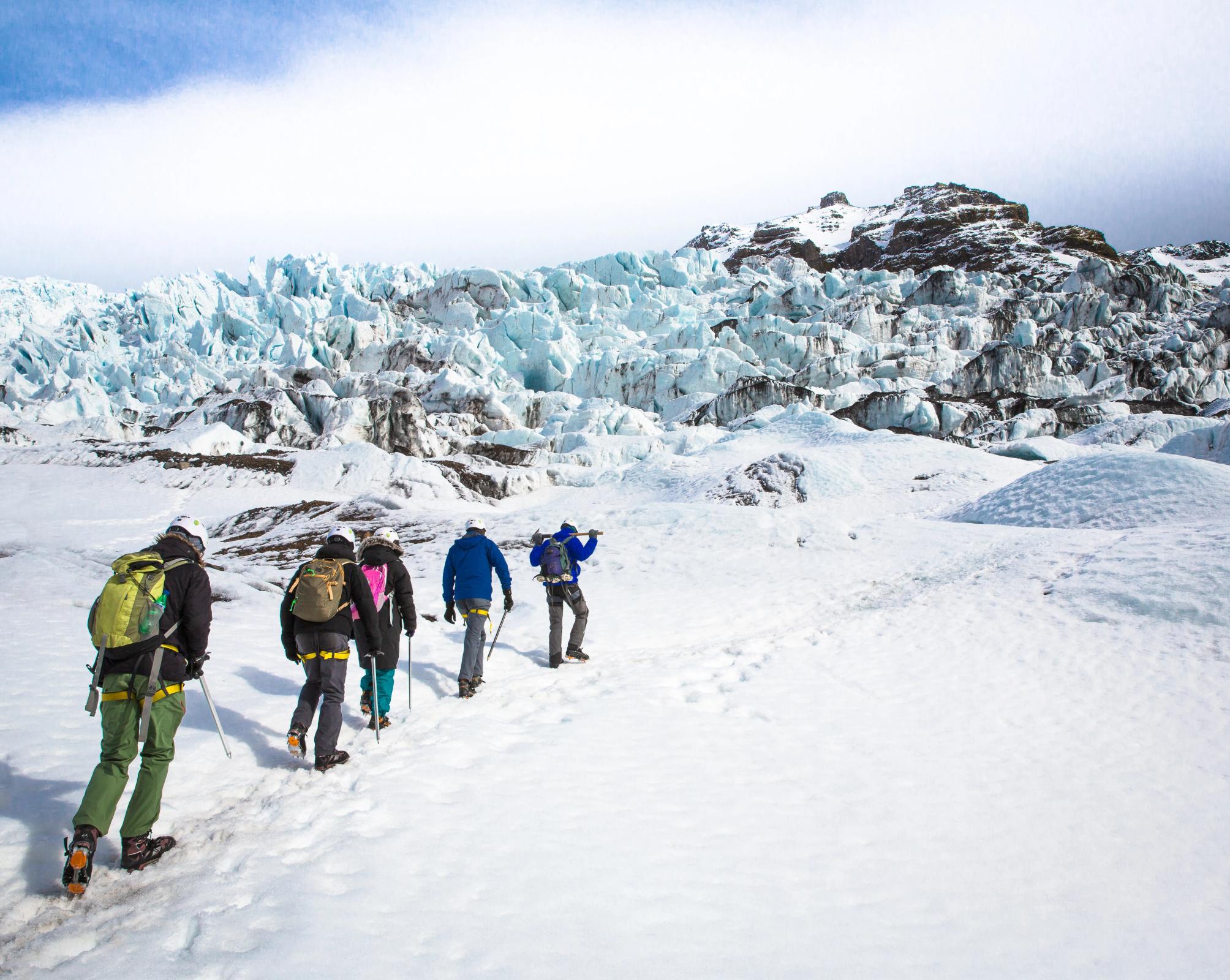 a group of people are walking in the snow near a glacier, Iceland
