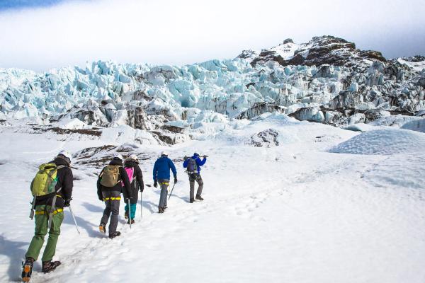 a group of people are walking in the snow near a glacier in iceland.