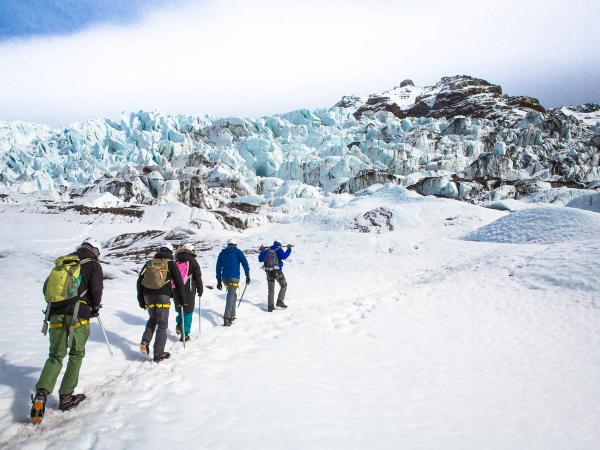 a group of people are walking in the snow near a glacier .