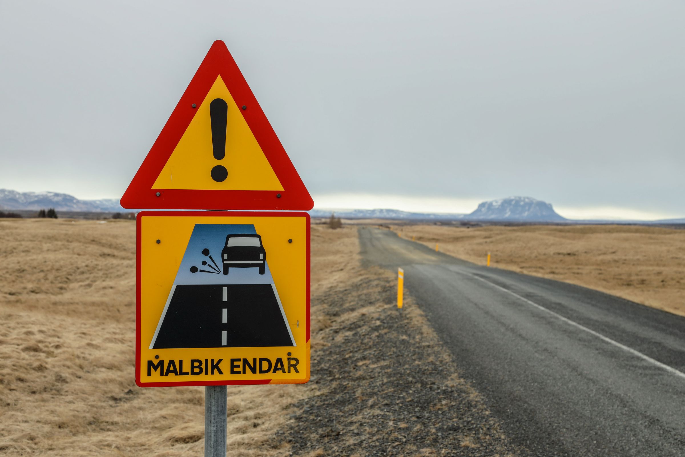 a yellow and red warning sign on the side of a road .