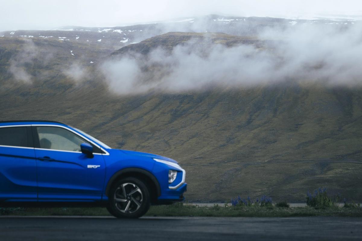 Vista lateral de un Mitsubishi Eclipse Cross aparcado, con nubes bajas descendiendo por la ladera de una montaña