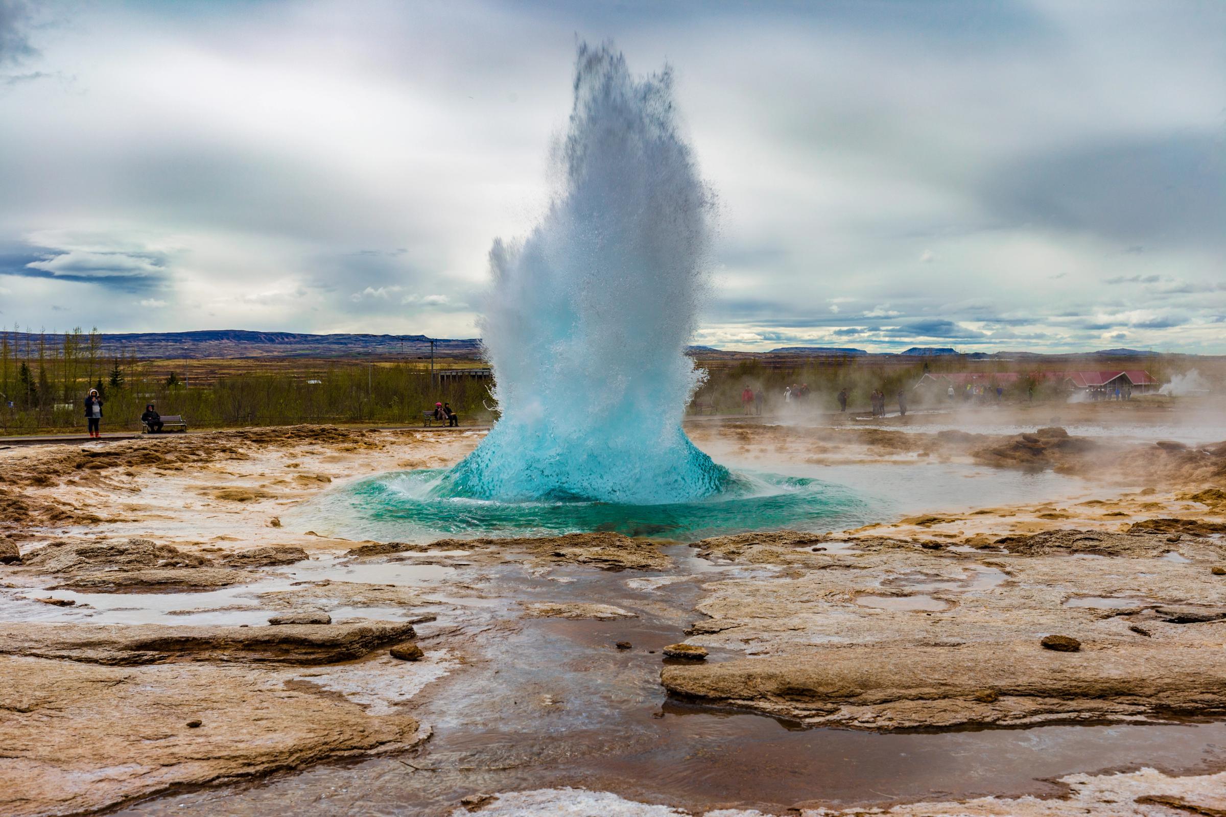 a blue geyser is erupting in the middle of a desert .