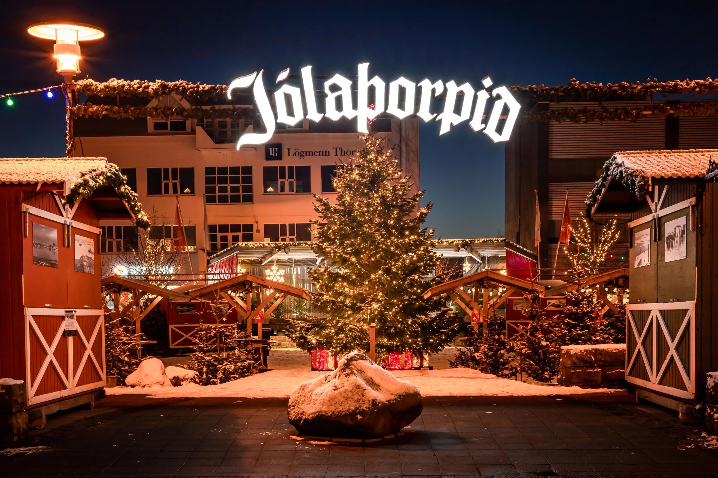 a christmas tree is lit up in front of a building at a christmas market .