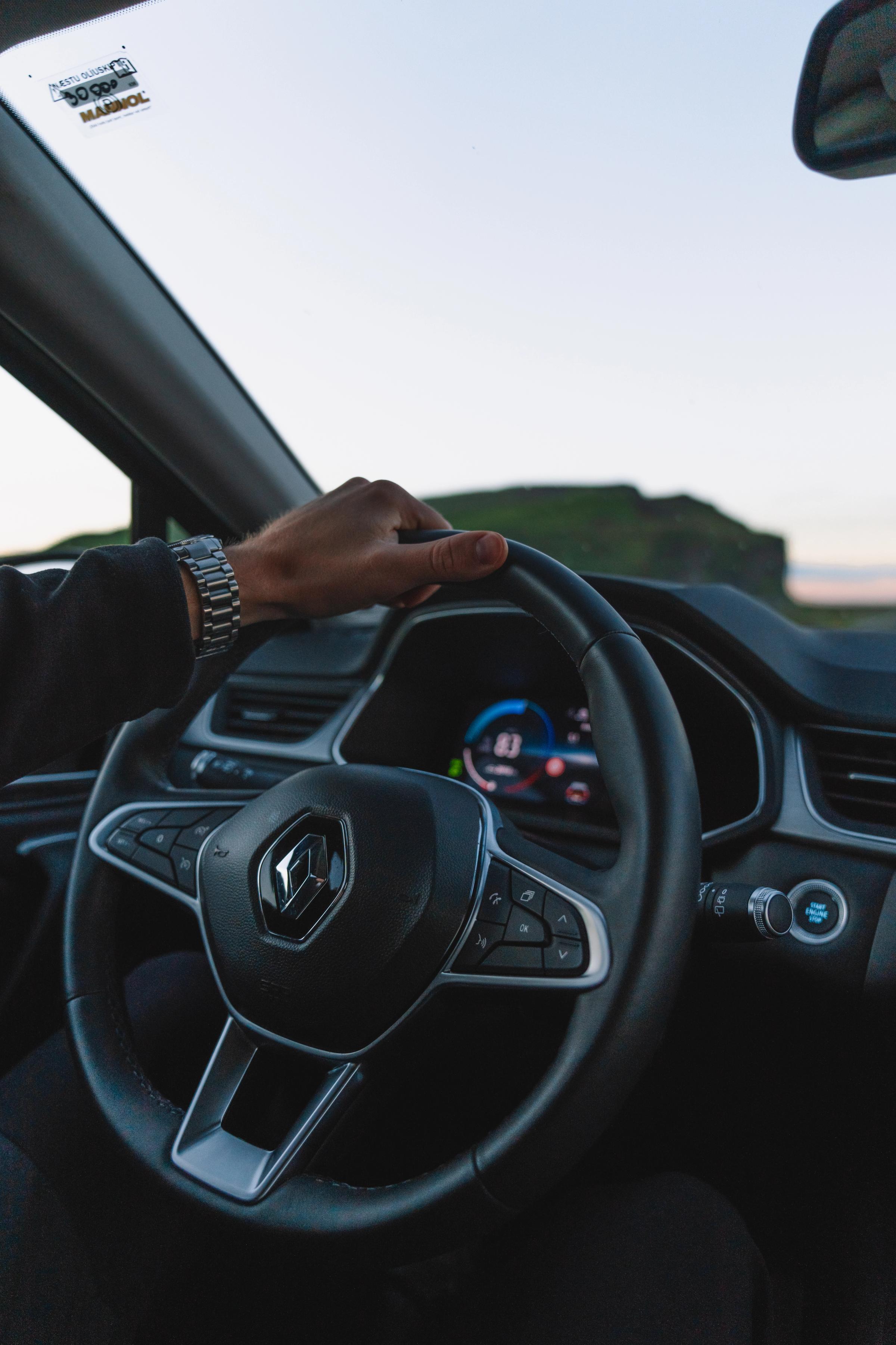 Mano en el volante del Renault Captur Volante de un Renault Captur con la mano del conductor apoyada y una colina costera visible en el exterior
