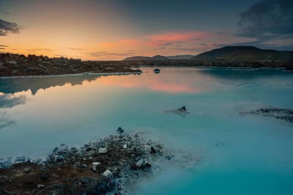 a large body of water surrounded by rocks and mountains at sunset .