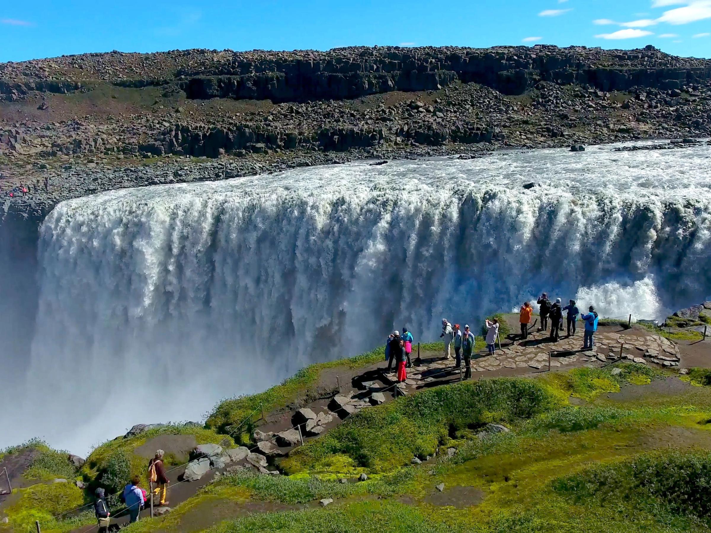 a group of people are standing on the edge of a waterfall .