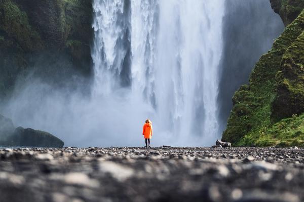 a man in an orange raincoat is standing in front of a waterfall in iceland.