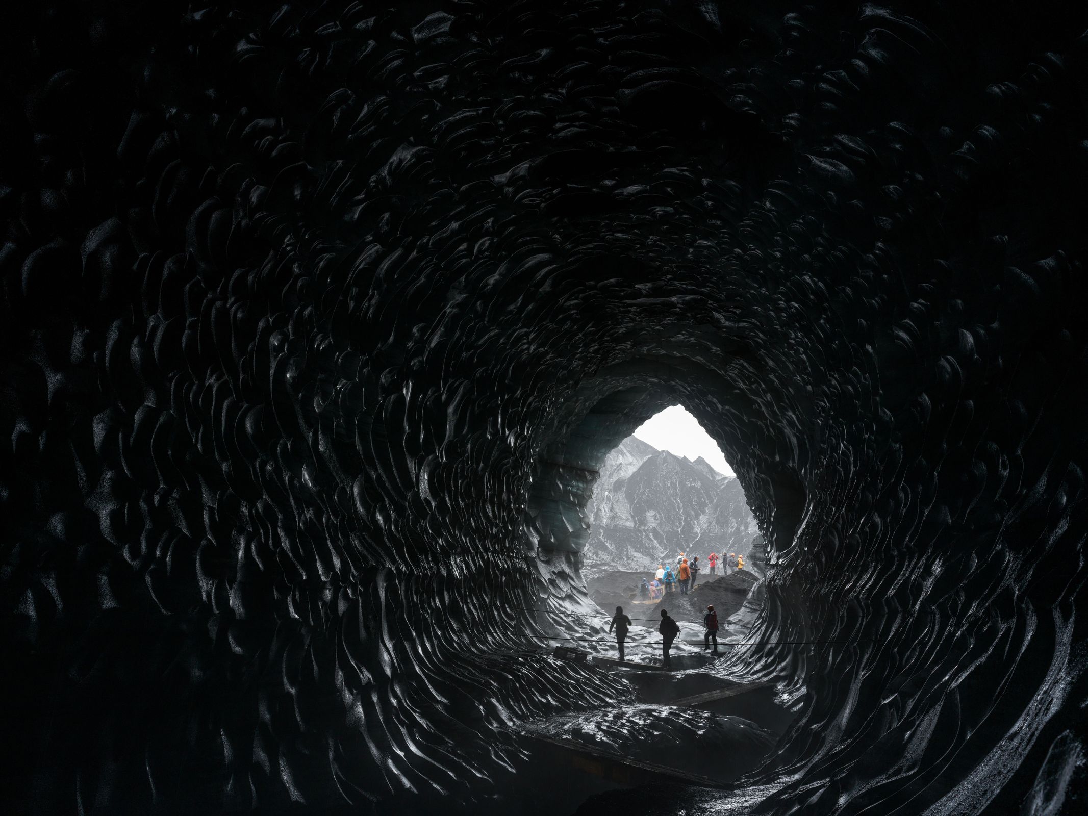 Three people exiting a dark ice cave