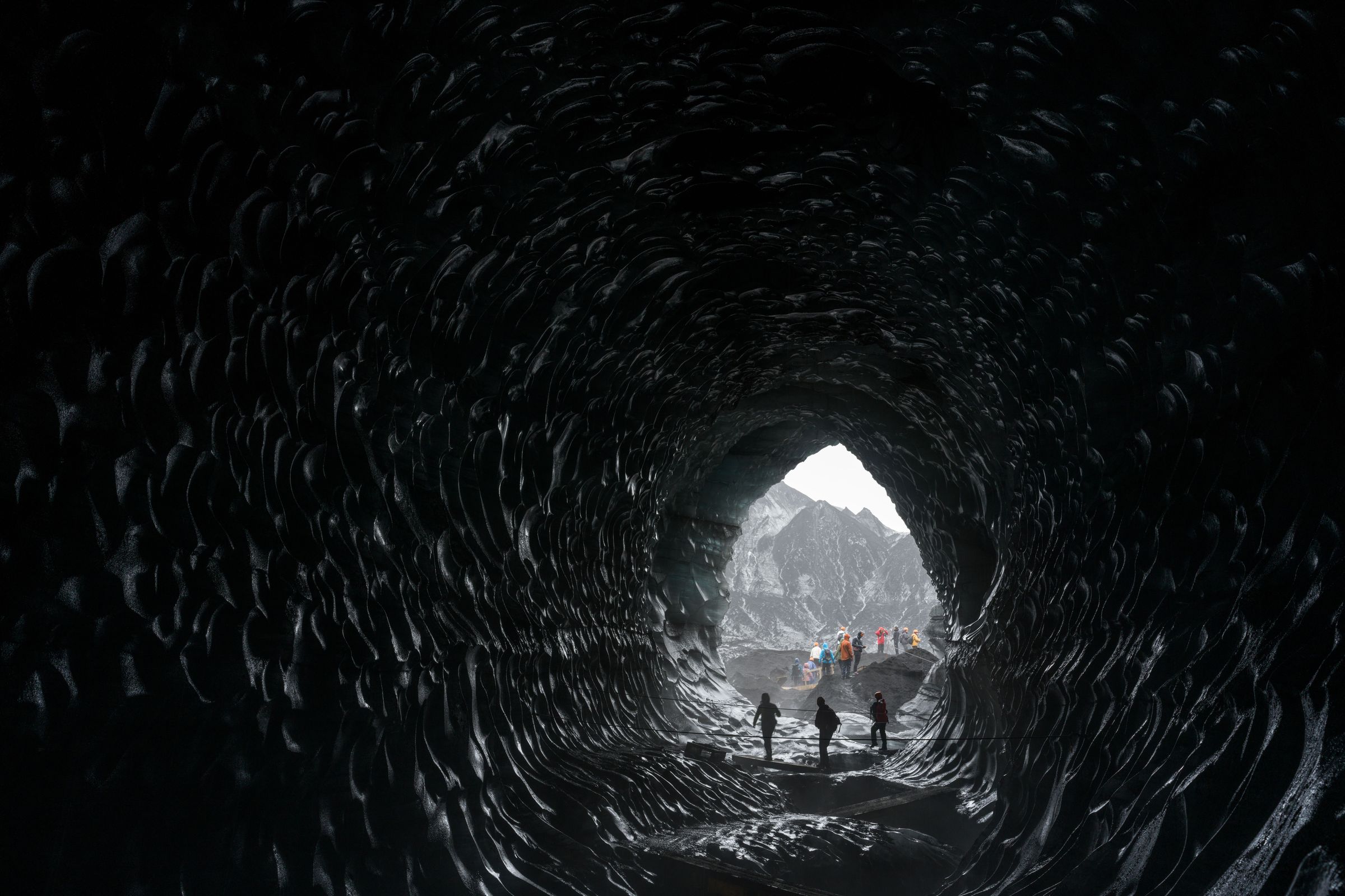 Three people exiting a dark ice cave