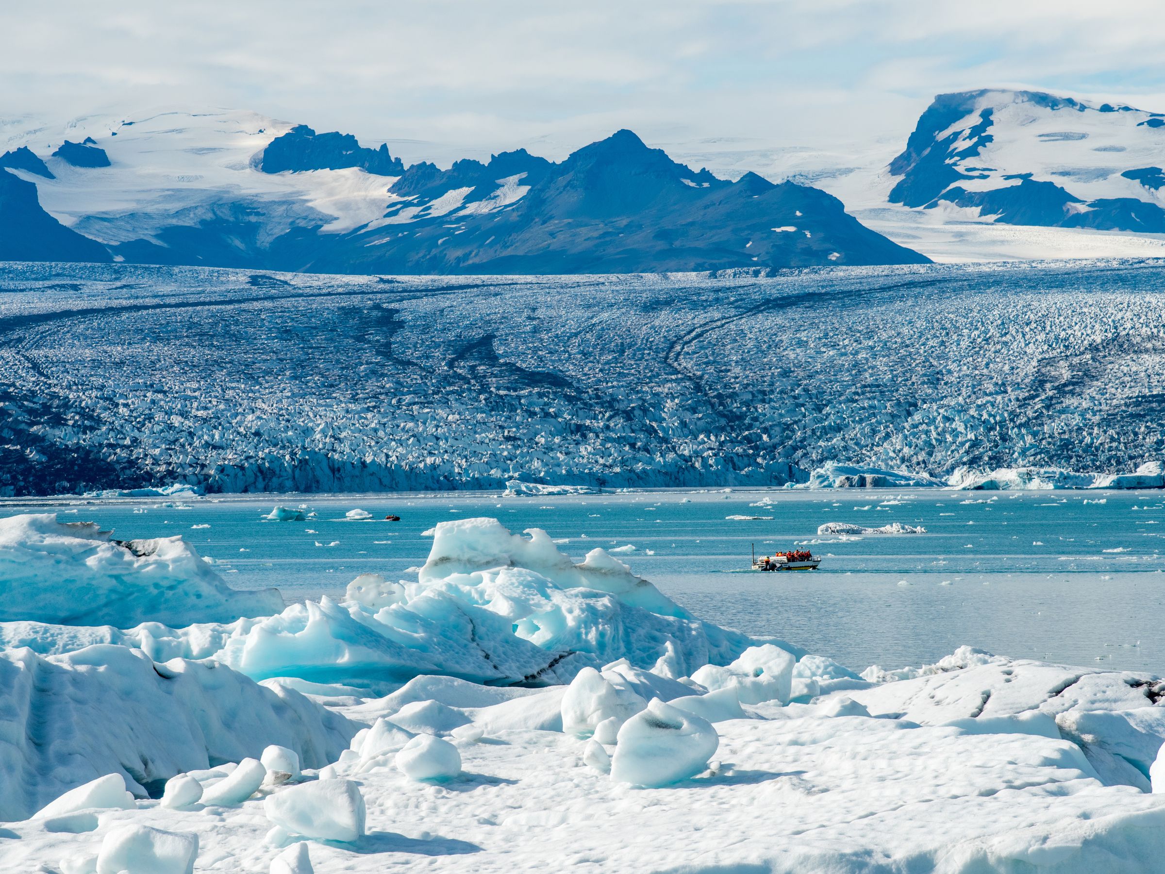 a boat is floating on top of a frozen lake with mountains in the background .