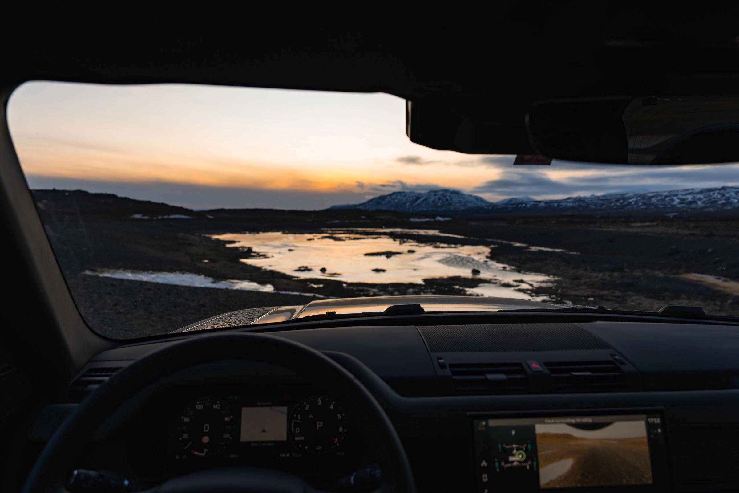 Vista de una puesta de sol islandesa sobre montañas nevadas desde el interior de un Land Rover Defender de alquiler de Go Car Rental