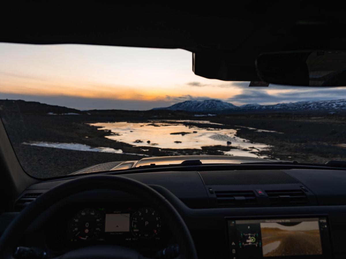 Vista del atardecer desde el interior del Land Rover Defender Vista de una puesta de sol islandesa sobre montañas nevadas desde el interior de un Land Rover Defender de alquiler de Go Car Rental