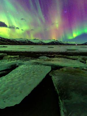 the aurora borealis is shining over a frozen lake .