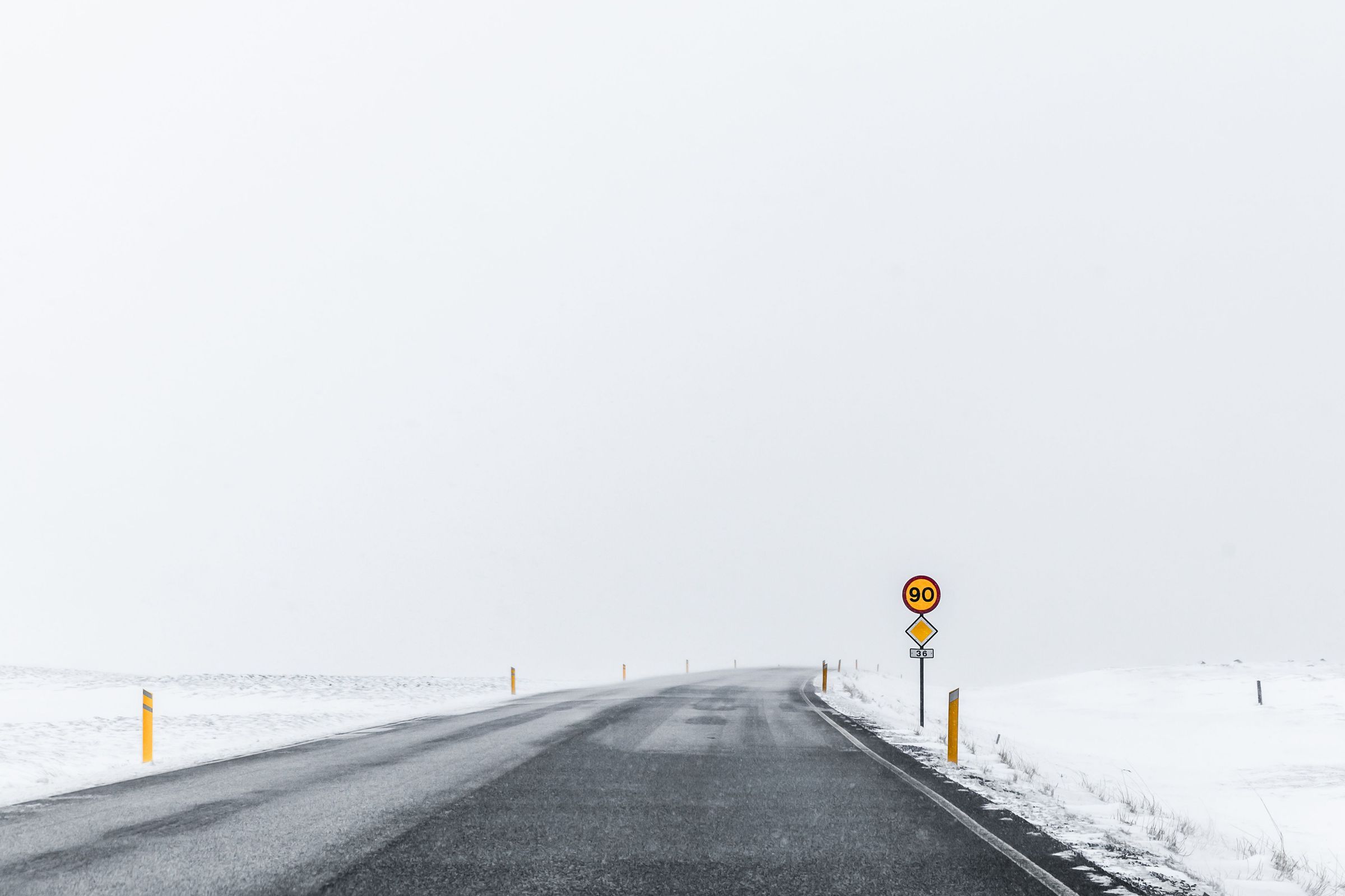 Navigating Iceland's wintry landscapes: a speed limit sign stands guard on a snowy road A paved snowy road in Iceland, marked by a speeding sign