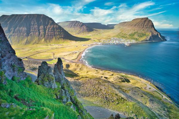 Panoramic view of a town nestled in a fjord, flanked by steep mountains and foreground cliffs.