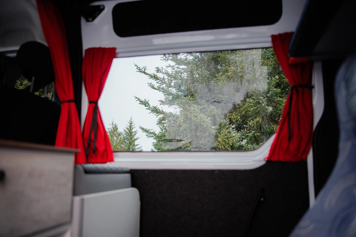 Seitenfenster mit roten, zurückgebundenen Vorhängen im Innenraum eines großen Wohnmobils für fünf Personen