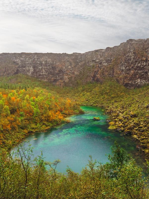 A vibrant blue-green lake surrounded by autumn foliage and tall, dark cliffs.