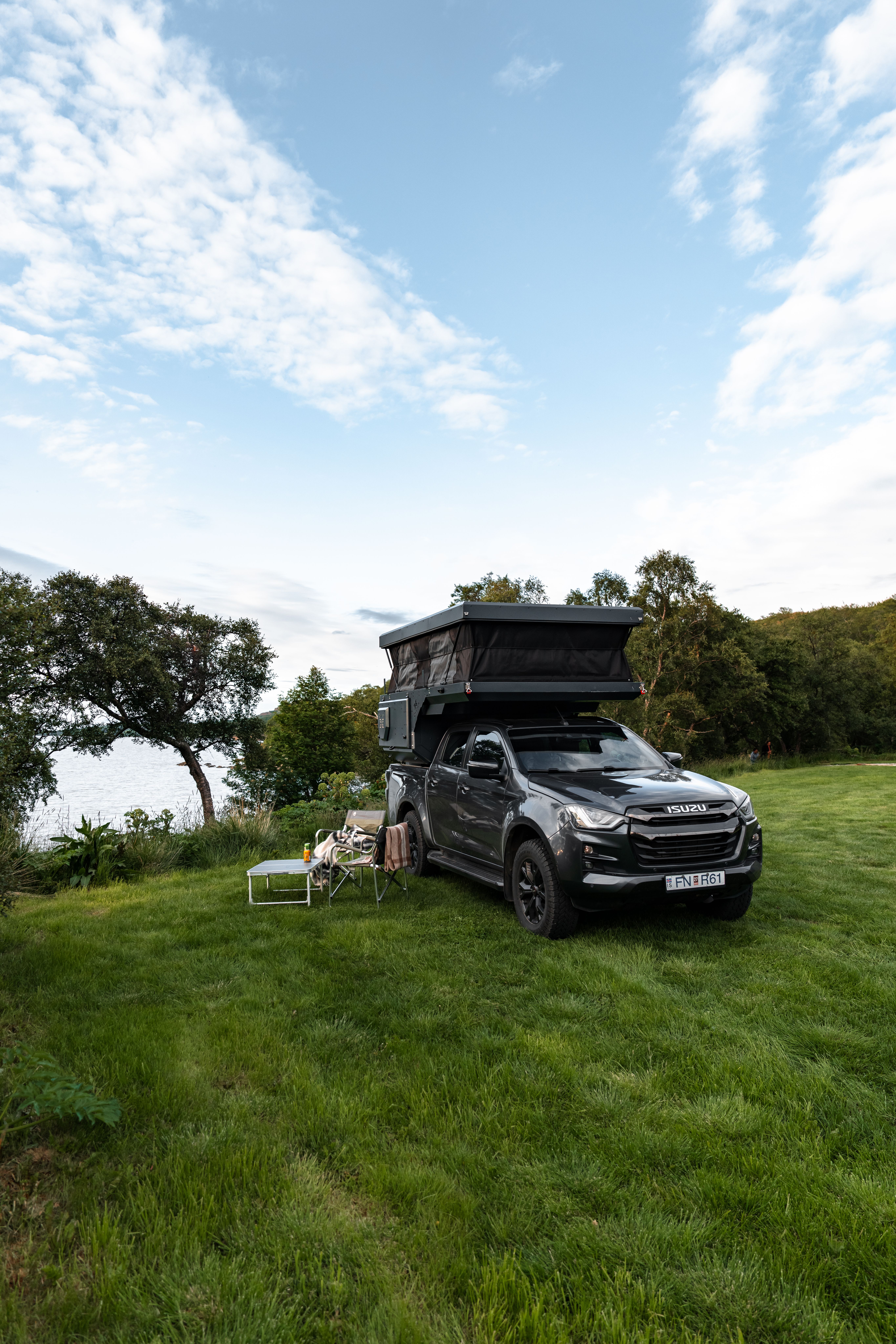 Cámper con techo elevable levantado junto a unas sillas y una mesa sobre el césped, alquiler de furgoneta cámper 4x4 en Islandia