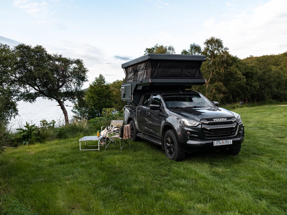 Montaje del campamento con techo elevable Cámper con techo elevable levantado junto a unas sillas y una mesa sobre el césped, alquiler de furgoneta cámper 4x4 en Islandia