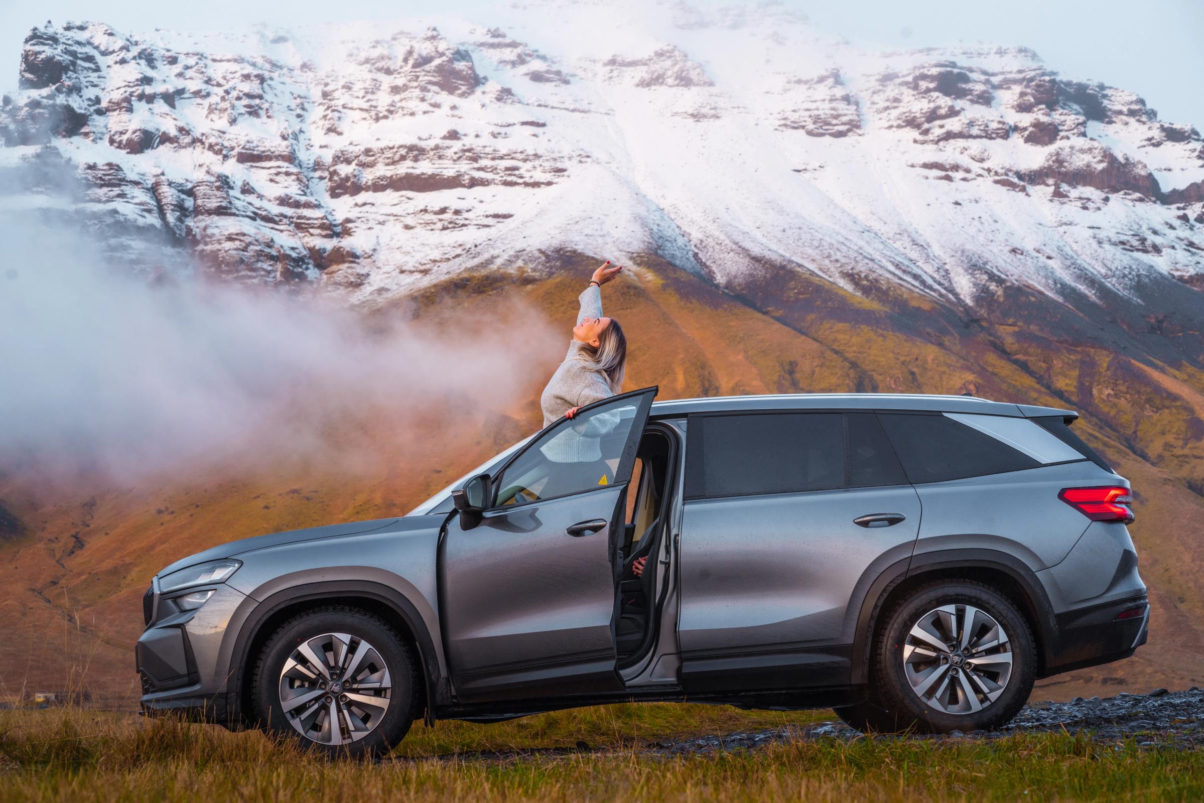 Vista do teto panorâmico do Skoda Kodiaq na montanha Vista lateral de um Skoda Kodiaq com a porta aberta e uma pessoa em pé no tejadilho, junto às montanhas