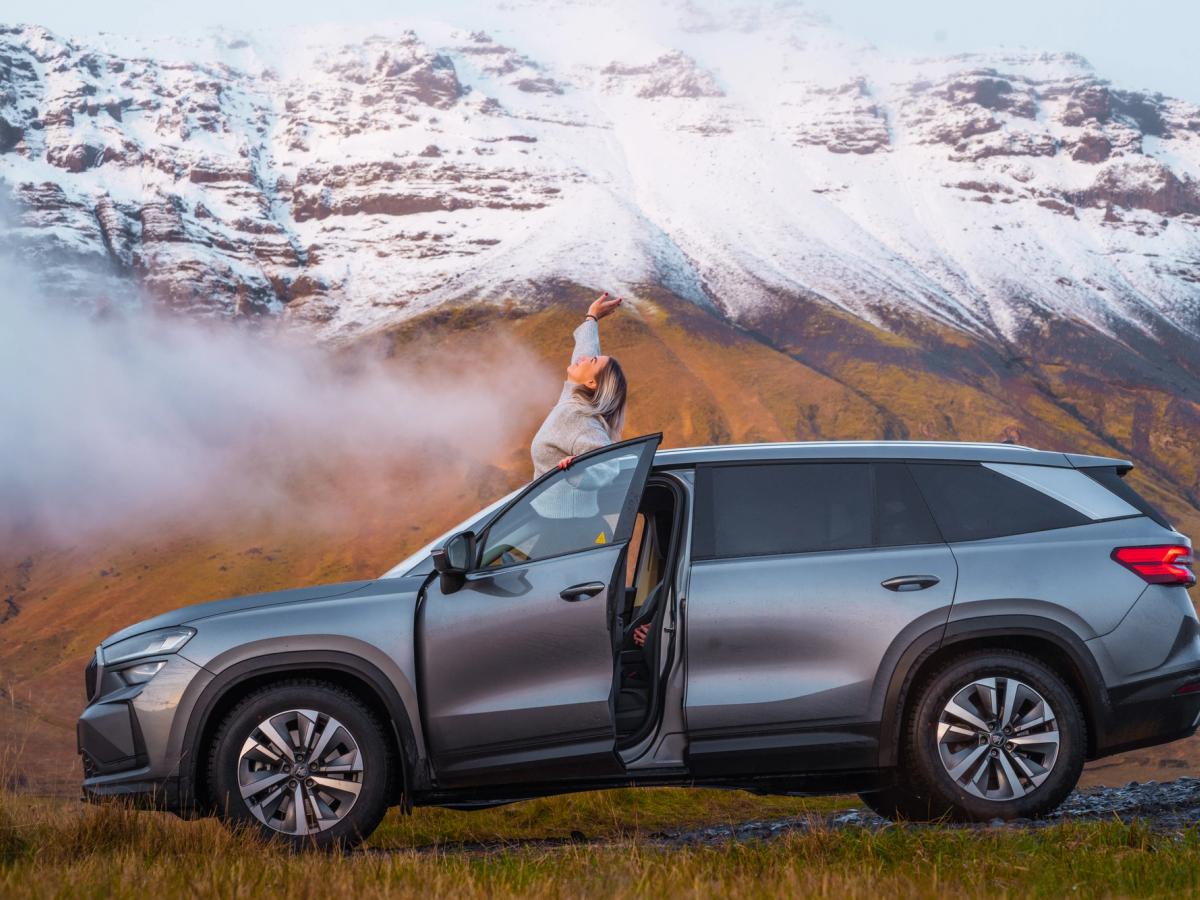 Vista do teto panorâmico do Skoda Kodiaq na montanha Vista lateral de um Skoda Kodiaq com a porta aberta e uma pessoa em pé no tejadilho, junto às montanhas