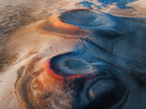 Orange and blue crater formations in a barren landscape.